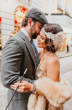 a man and woman standing next to each other in front of a building with christmas lights