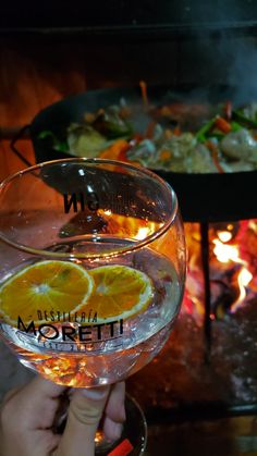 a person holding up a wine glass in front of a fire place with food on it