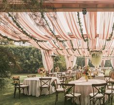 an outdoor dining area with tables and chairs covered in pink draping, surrounded by greenery