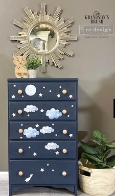 a blue dresser with stars and clouds painted on the drawers next to a potted plant