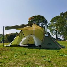 a tent set up in the middle of a field with grass and trees around it