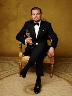 a man in a tuxedo sitting on a chair holding an oscar for best supporting actor