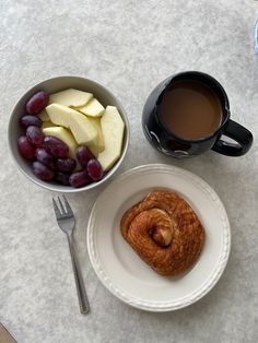 a bowl of fruit next to a cup of coffee and a plate with a croissant