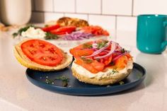 an open face sandwich with tomatoes and onions on a blue plate next to a coffee mug