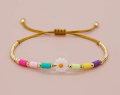 a bracelet with beads and a flower on the end is sitting on a pink surface