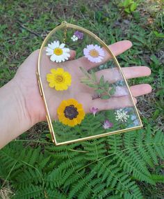 a person's hand is holding a glass case with flowers in it and plants inside