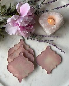 pink flowers are sitting on a marble plate next to a candle and some glass vases