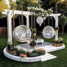 an outdoor seating area with hanging chairs and flowers on the grass, in front of a fence