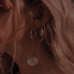 a woman with long blonde hair wearing large earrings and pearls on her ear, looking down at the ground