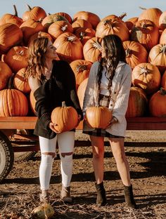 two women standing next to each other with pumpkins in the background