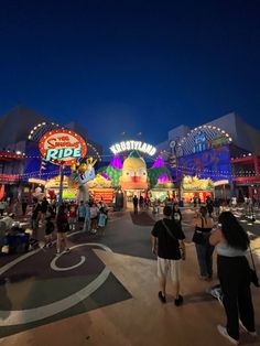 the entrance to an amusement park at night with lots of people walking around and riding on roller coasters