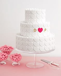 a three tiered white cake with hearts on it and pink candies in the foreground