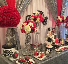 a table topped with red and white flowers next to tall vases filled with cake