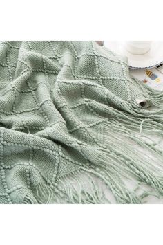 a green blanket sitting on top of a bed next to a cup and saucer