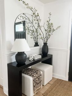 a black and white console table with two vases on it next to a mirror