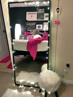 a mirror with lights on it in the corner next to a white rug and pink blanket