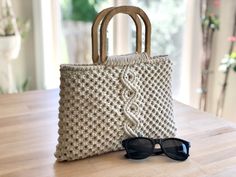 a knitted bag sitting on top of a wooden table next to some sunglasses and a pair of glasses