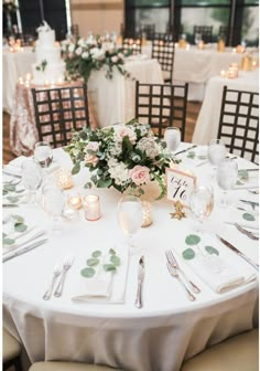 the table is set with white linens, silverware and greenery for an elegant wedding reception