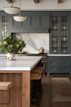 a kitchen with gray cabinets and marble counter tops, an island in between two stools