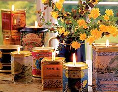 several tea tins with candles in them on a table next to flowers and a window