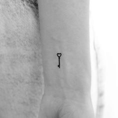 a small black key tattoo on the left inner arm, with a tiny heart at the end