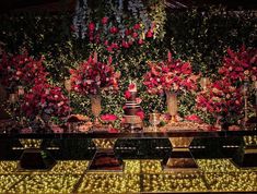 a table topped with lots of flowers and candles next to a wall covered in greenery