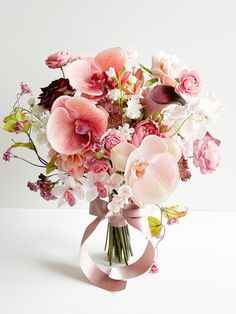 a bouquet of pink and white flowers in a vase with a ribbon on the side