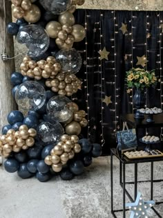 a table topped with lots of balloons next to a black and gold wall hanging from it's side