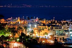 the city is lit up at night by the ocean