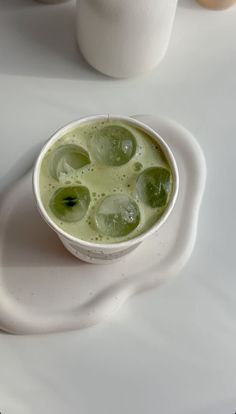 a white bowl filled with green liquid on top of a white plate next to eggs