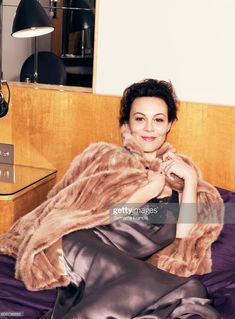 a woman sitting on top of a bed wearing a fur coat