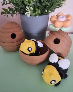 three little toy bees sitting next to a potted plant and some fake flowers on a table