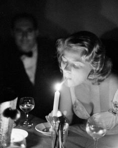 a woman sitting at a table with a lit candle in her hand and another man standing behind her