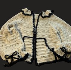 a crocheted jacket with black trims and bows on the collar is shown