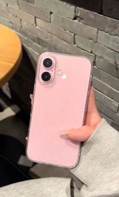 a person holding up a pink iphone case in front of a brick wall and table