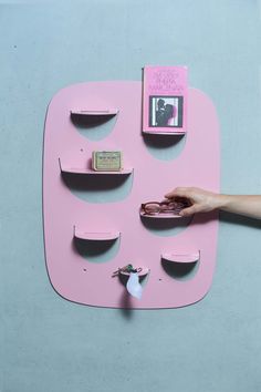 a pink shelf with shelves on it and a hand reaching for the one in front