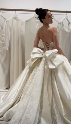 a woman in a wedding dress is looking at the back of her gown, which has been made from satin and lace