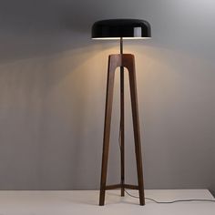 a wooden floor lamp with a black shade on the base and a white light behind it