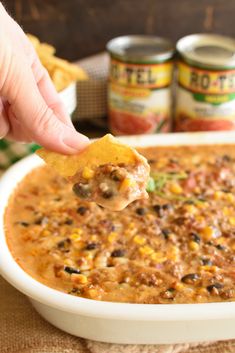 a hand holding a tortilla chip over a bowl of chili cheese dip