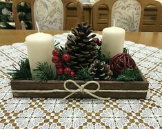 a wooden tray filled with candles and pine cones on top of a dining room table