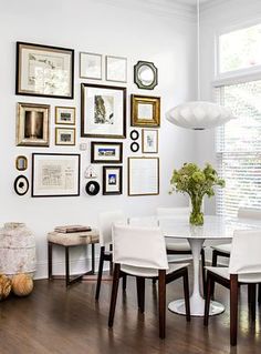 a dining room table with white chairs and pictures on the wall in front of it