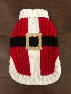 a red and white knitted dog sweater with a santa clause design on it's chest