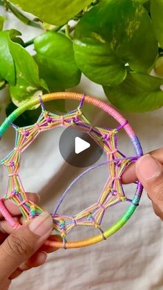 two hands are holding a colorful piece of string art that looks like a circular object