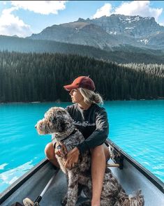 a woman is sitting in a boat with her dog on the water and mountains behind her