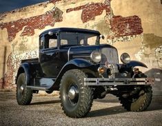 an old black truck parked in front of a brick building with graffiti on it's walls