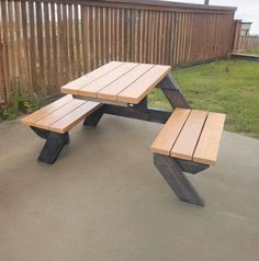 a wooden picnic table sitting on top of a cement floor next to a fenced in area