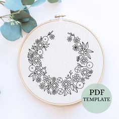 a cross stitch hoop with flowers and leaves on it, next to a green plant