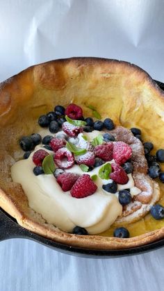 a pancake with berries and cream on top is sitting in a pie dish, ready to be eaten