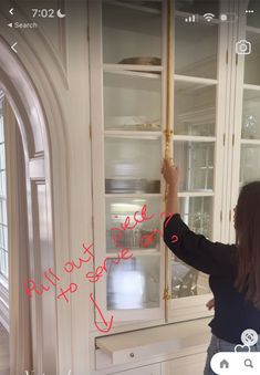 a woman standing in front of a white china cabinet with red writing on the glass door