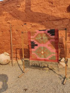 a pink and green rug sitting on top of a dirt field next to a stone wall